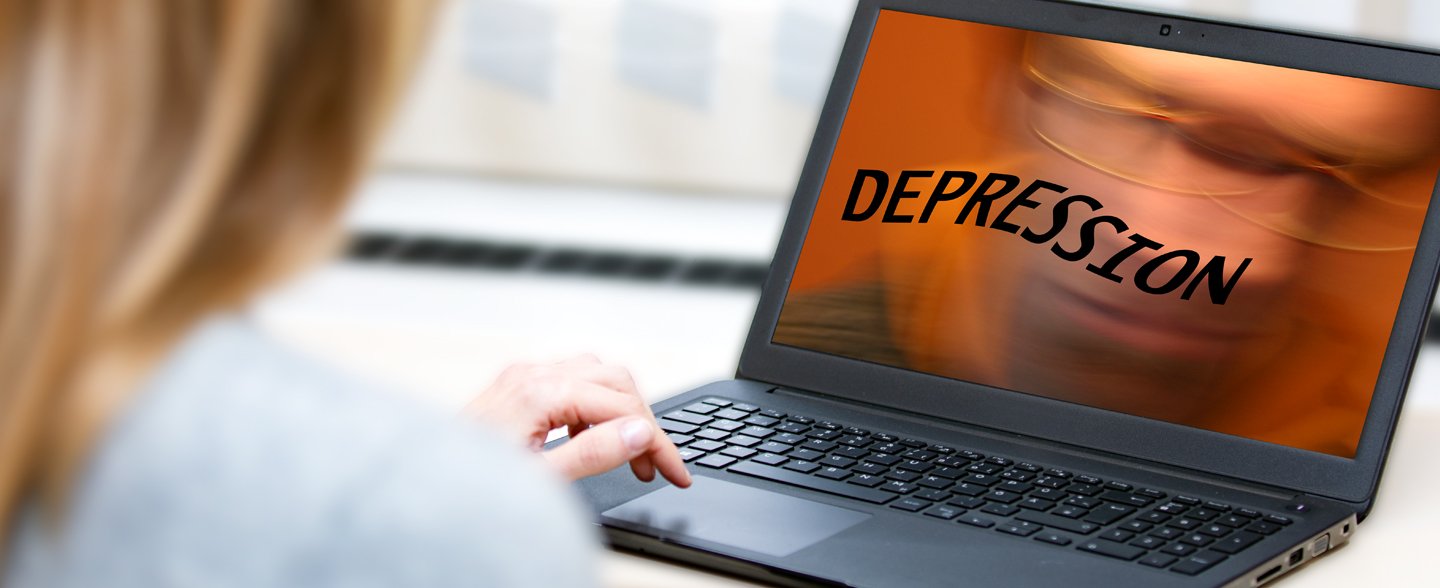 Das Symbolbild zeigt eine Frau von hinten, die vor einem Laptop an einem Tisch sitzt. Auf dem Bildschirm steht in schwarzen Buchstaben das Wort Depression.