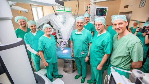 A group of men in surgical scrubs is standing next to a surgical robot. 