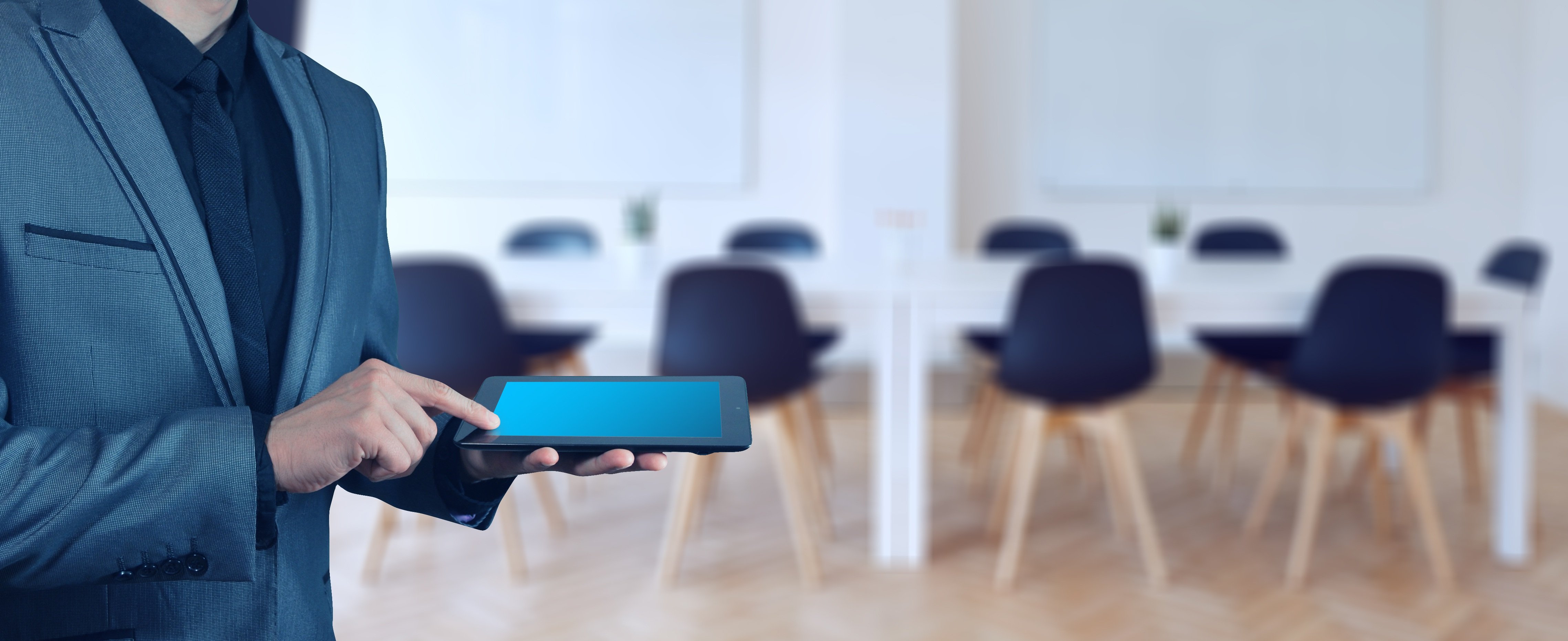 Konferenzraum Mann mit Tablet, im Hintergrund Konferenztisch mit Stühlen