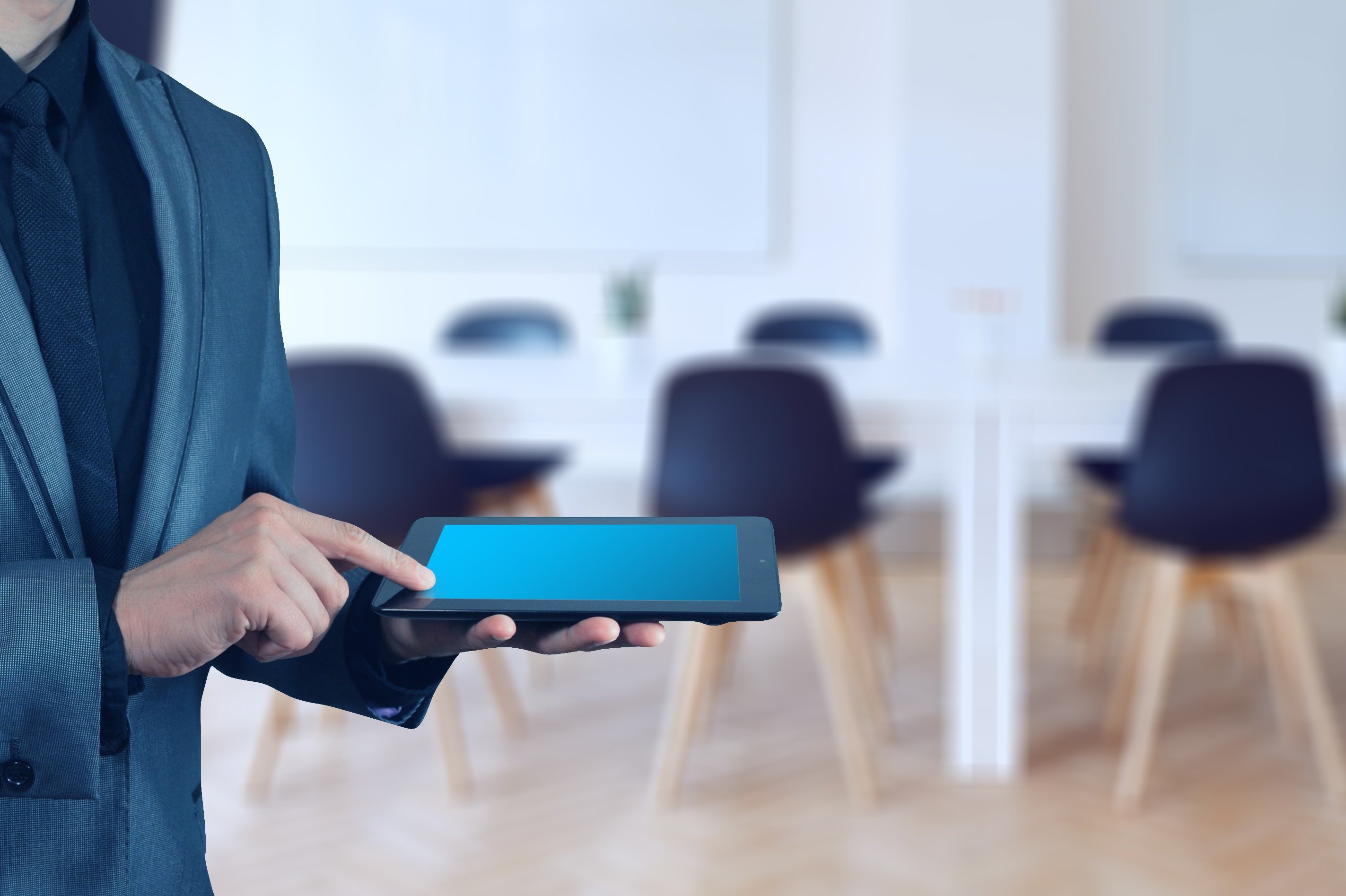 Mann mit Tablet, im Hintergrund Konferenztisch mit Stühlen