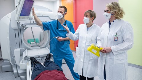 Professor Dr. Dr. Anette Melk stands with PRACTIS participants Dr. Johanna Diekmann and Dr. Carl Grabitz during an examination situation in MHH nuclear medicine at a special imaging device.