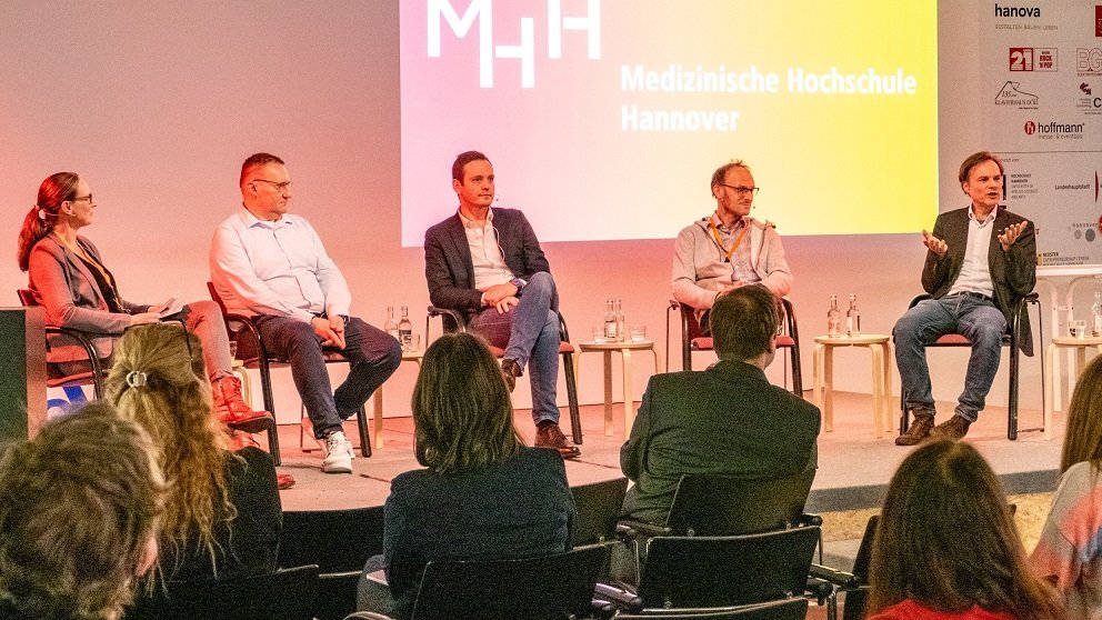 Fünf Menschen sitzen auf Stühlen auf einem Podium im aufhof, vor ihnen sitzen mehrere Menschen in Stuhlreihen. 