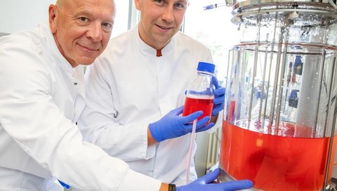 Zwei Forscher in weißen Kitteln stehen in einem wissenschaftlichen Labor vor einem Rührkessel-Bioreaktor