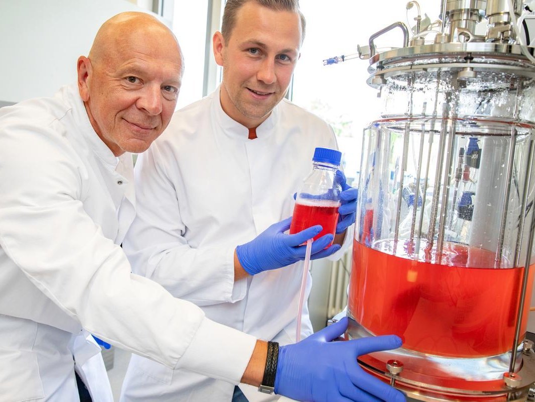 Zwei Forscher in weißen Kitteln stehen in einem wissenschaftlichen Labor vor einem Rührkessel-Bioreaktor
