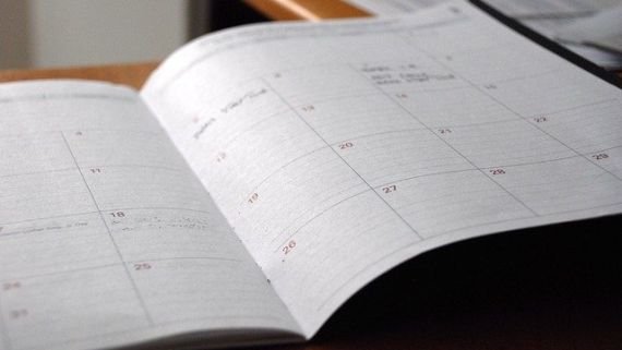 Ein Kalender in Heftform liegt aufgeschlagen auf einem Tisch. Man sieht die verschiedene Kästchen für die einzelnen Tage mit Datum.