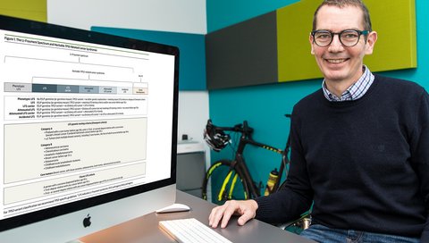 MHH-Professor Dr. Christian Kratz steht an einem Tisch mit einem PC-Bildschirm, auf dem das Klassifikationsmodell für das Li-Fraumeni-Syndrom zu sehen ist. 