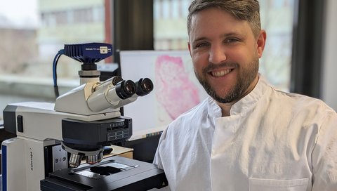 Dr. Jonas Schupp sitzt neben einem Mikroskop. 