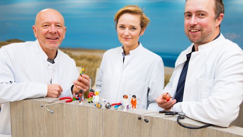 The photo shows Professor Dr Nico Lachmann, spokesperson for the new training programme nextGENERATION, with co-spokespersons Professor Dr Christine Happle (centre) and Dr Robert Zweigerdt (left). They are standing behind a balustrade on which small figures can be seen that are meant to symbolise people in the hospital, as well as small objects from the laboratory. This is meant to represent the networking of research and clinic, which this new training course strongly advocates