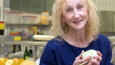 MHH-Ernährungsexpertin Sonja Nothacker sitzt in einer Lehrküche mit einem Kohlrabi in der Hand auf einem Tisch. 