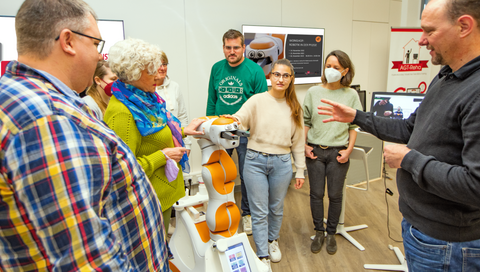 Mehrere Menschen stehen um Assistenzroboter Lio herum. 