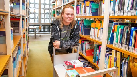 Paul Vinke steht in der Bibliothek angelehnt an einen Bücherwagen