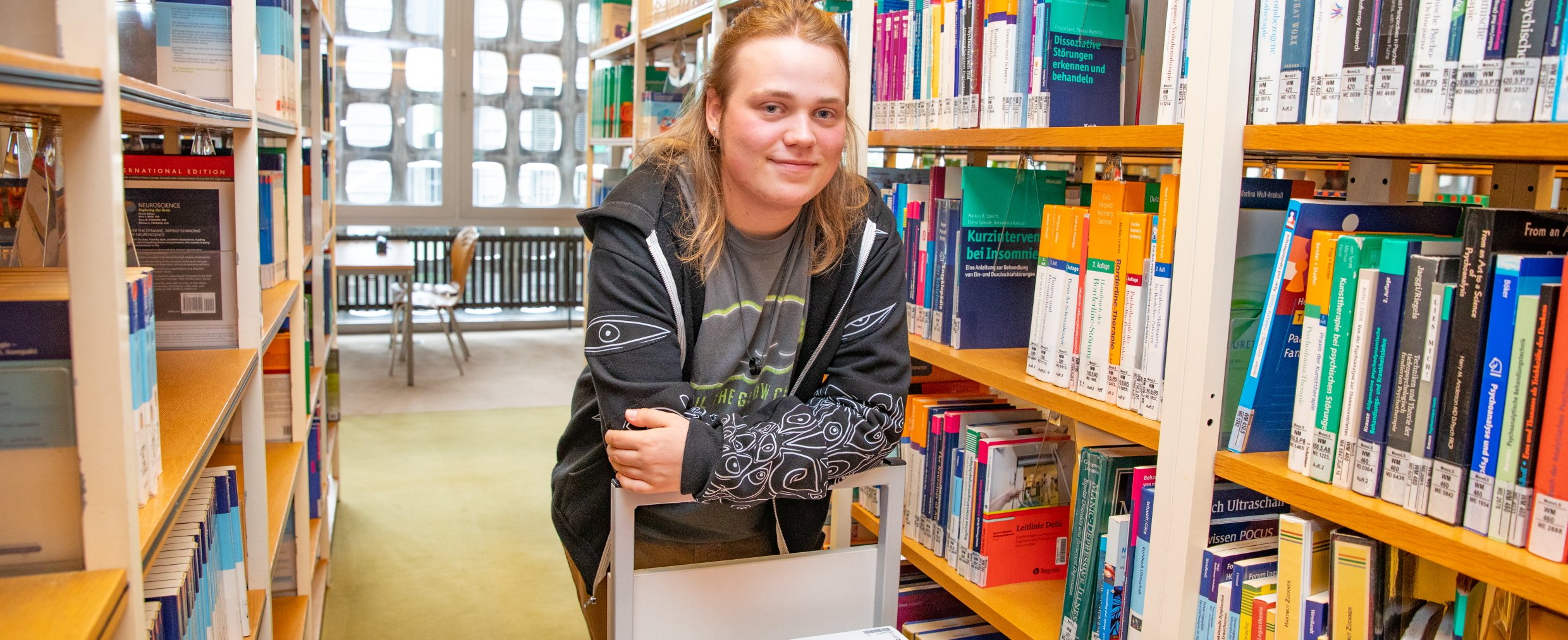 Paul Vinke steht in einem Gang der MHH-Bibliothek mit Bücherregalen.