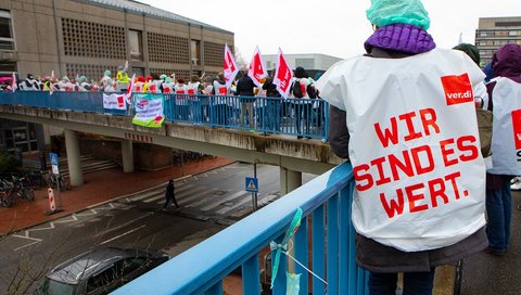 Archivbild zeigt streikende Mitarbeitende mit Verdi-Fahnen, die auf einer Hochbrücke auf dem MHH-Campus stehen. 
