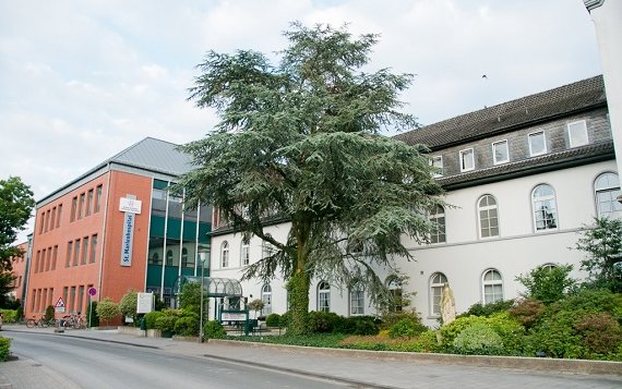 Eine Asphaltstraße, rechts davon ein rotes und ein weißes Gebäude. Beide hängen zusammen. Am roten Gebäude steht St. Marienhospital.