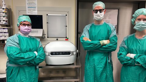 Männer und Fraun stehen in Kitel neben einer Maschine