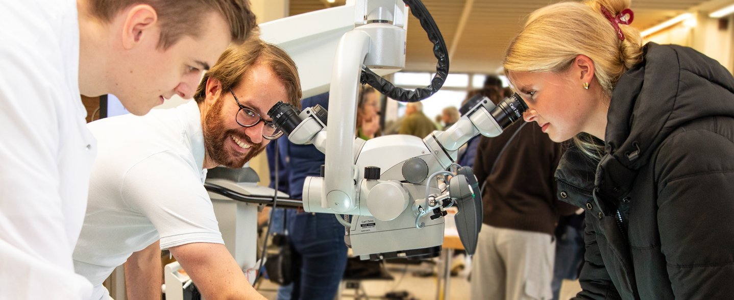 Eine junge Frau schaut durch ein Mikroskop. 