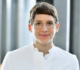 Porträtbild von Lisa Sandmann, die einen weißen Arztkittel trägt. 