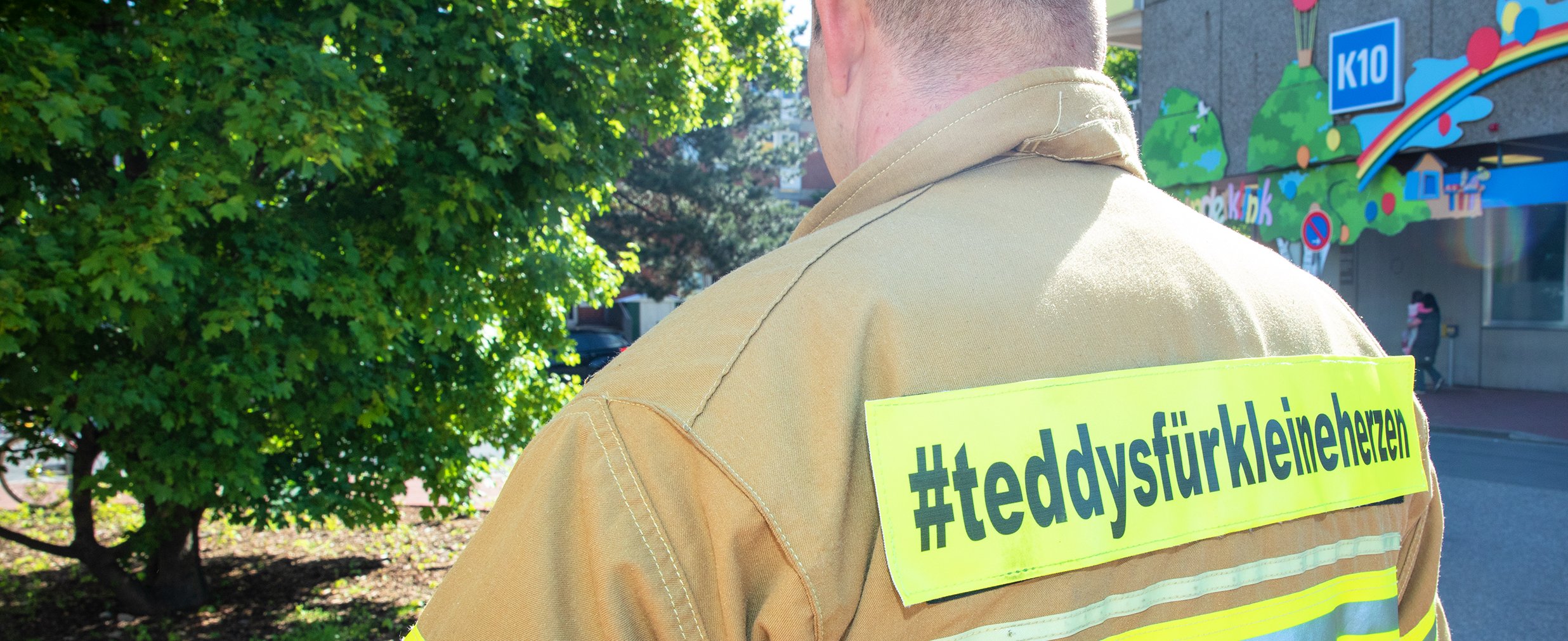 Feuerwehrmann von hinten mit der Aufschrift auf der Jacke "#teddysfürkleineherzen"