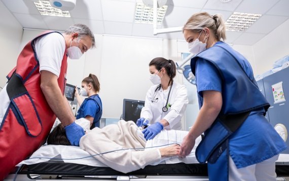 Copyright: Marienhospital Osnabrück Vier Personen mit Masken, drei von ihnen mit Röntgenschürzen und eine mit Kittel, stehen um einen Patienten, der auf eine Liege liegt.