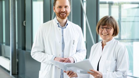 Auf dem Foto sind Dr. Hümmert und Professorin Trebst, in einem Gang der MHH stehend, zu sehen. 