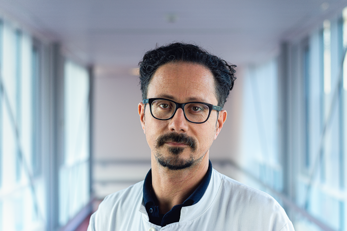 Porträtbild von Bastian Ringe, der einen weißen Arztkittel und eine Brille trägt.
