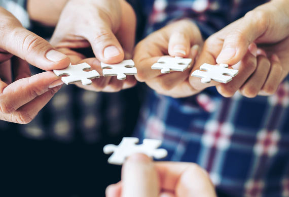 Fünf in die Mitte ausgestreckte Hände. Jede Hand hält ein Puzzleteil.