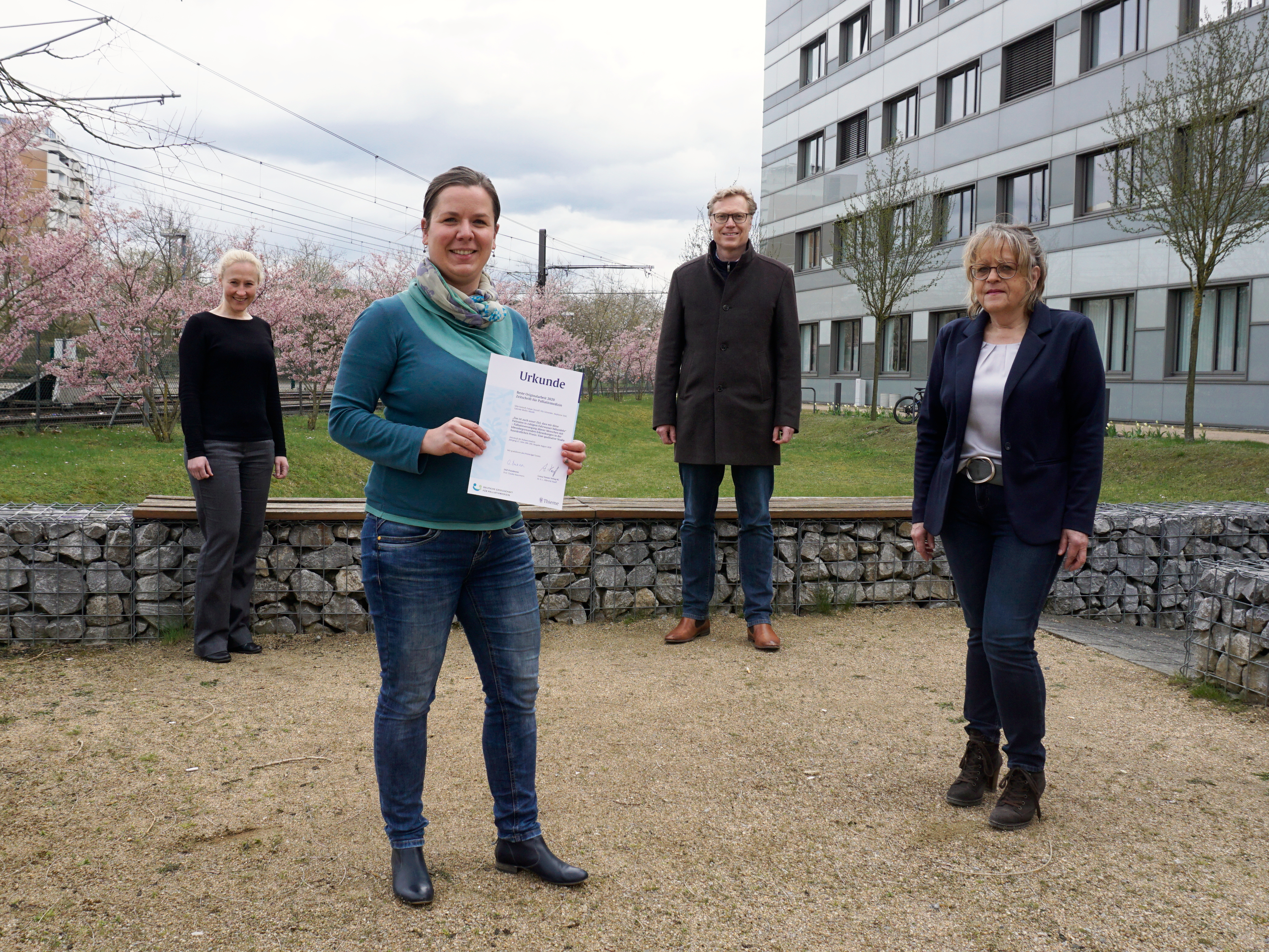 Drei Autorinnen und ein Autor der beiden ausgezeichneten Originalarbeiten stehen im Außenbereich des MHH-Geländes. Die Autorin Silke Freihoff hält eine Urkunde.