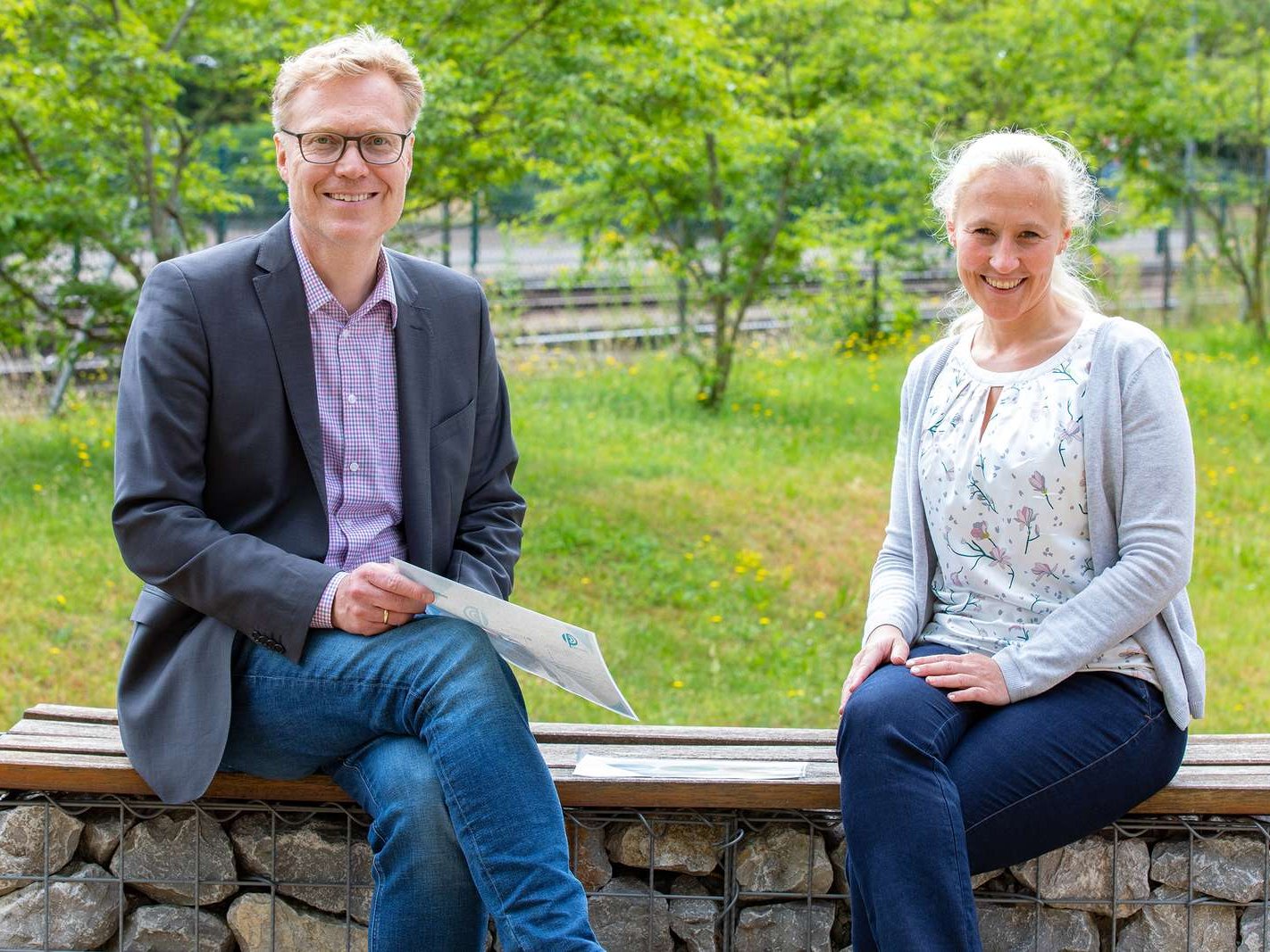 Professor Dr. Nils Schneider und Professorin Dr. Stephanie Stiel sitzen draußen zusammen auf einer Bank.