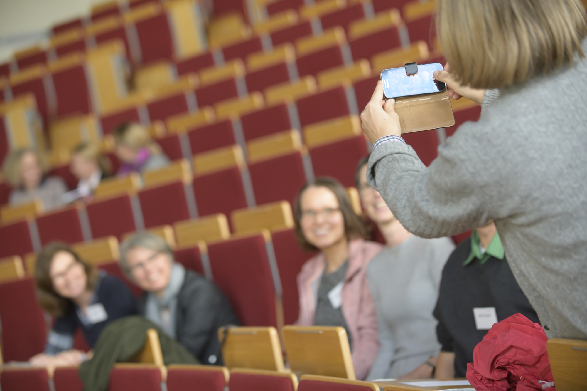 Eine Frau fotografiert mit ihrem Handy mehrere Personen in Hörsaal F.
