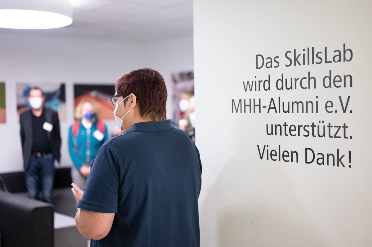 Blick über die Schulter der Referentin in die Menschenmenge, im Vordergrund ein Hinweis darauf, dass das Skills Lab finanziell vom MHH-Alumni e.V. unterstützt wird.