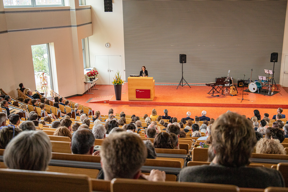 Über die Köpfe der Gäste hinweg sieht man unten auf der Bühne Frau Dr. Renneberg