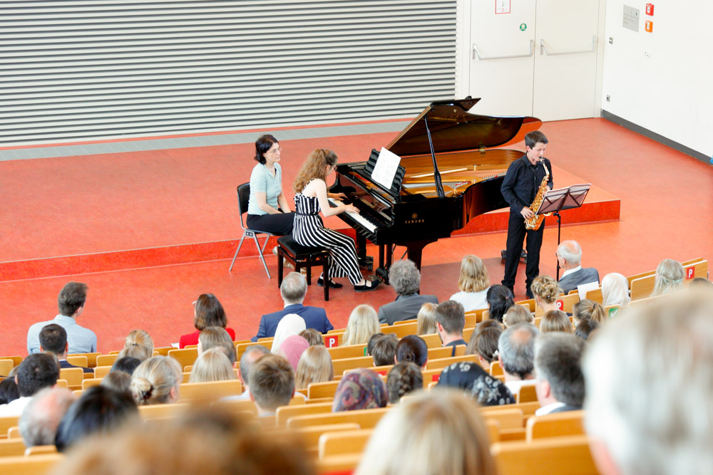 Über die Köpfe des Publikums hinweg sieht man unten im Hörsaal die Musiker:innen.