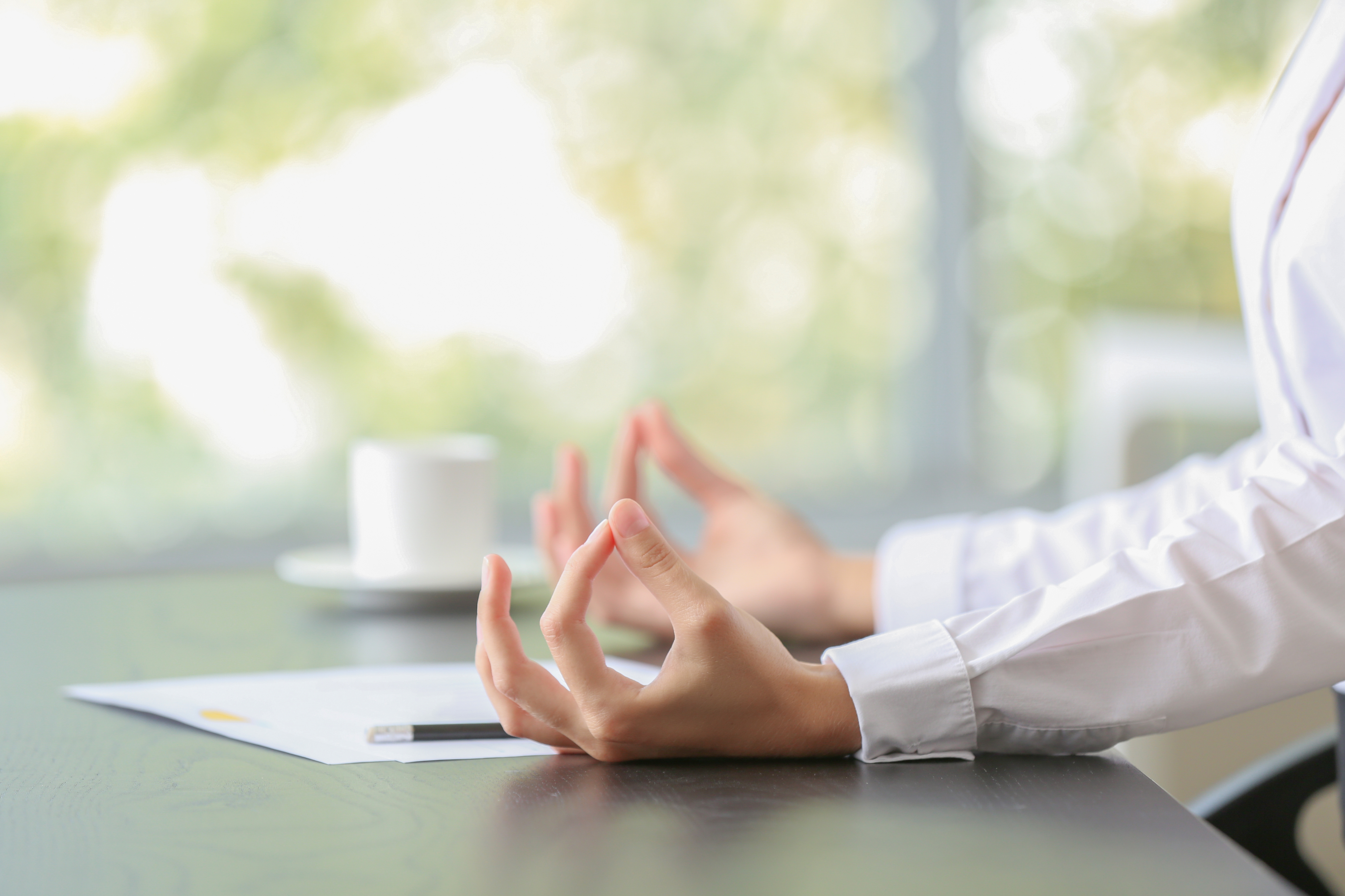 Copyright: Adobe Stock zwei Hände liegen auf dem Schriebtisch und formen die Yoga-Handgeste Rudra Mudra (auch Solarplexus-Handgeste genannt)