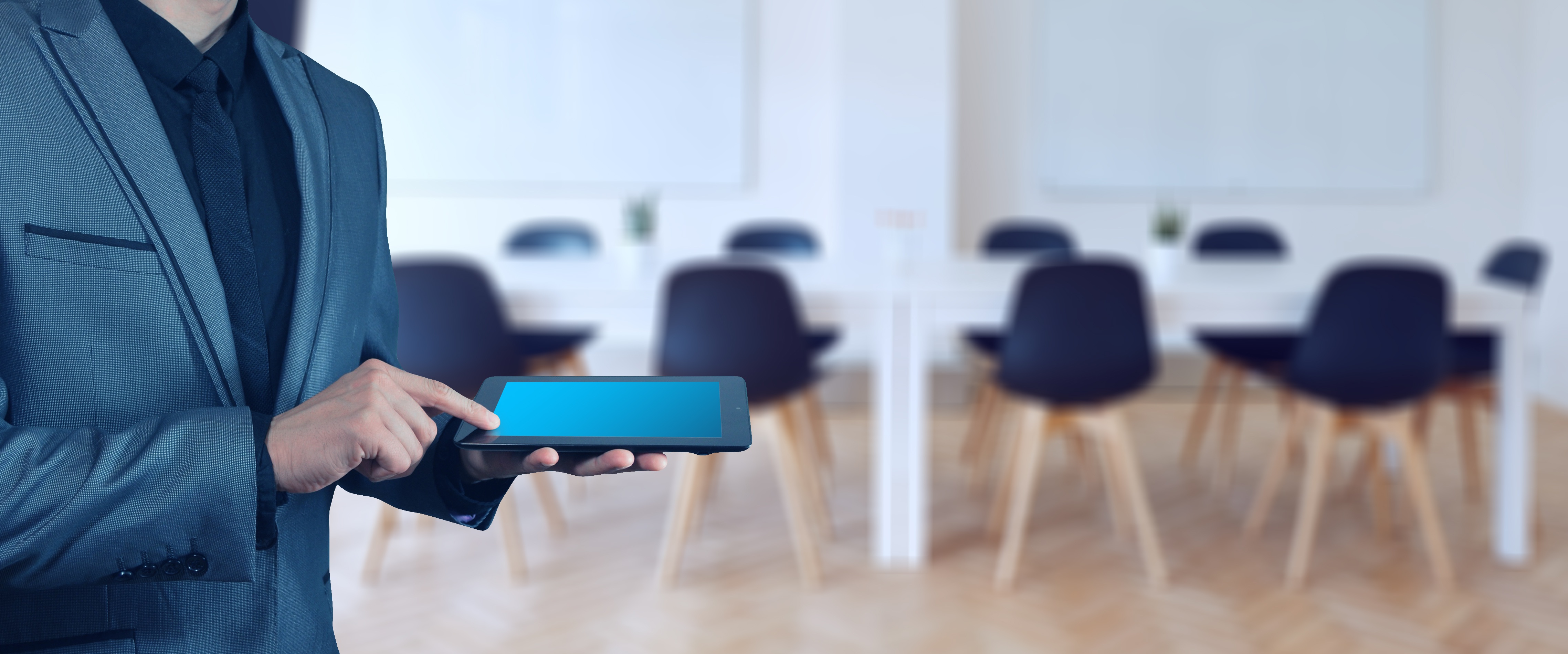 Konferenzraum Mann mit Tablet, im Hintergrund Konferenztisch mit Stühlen