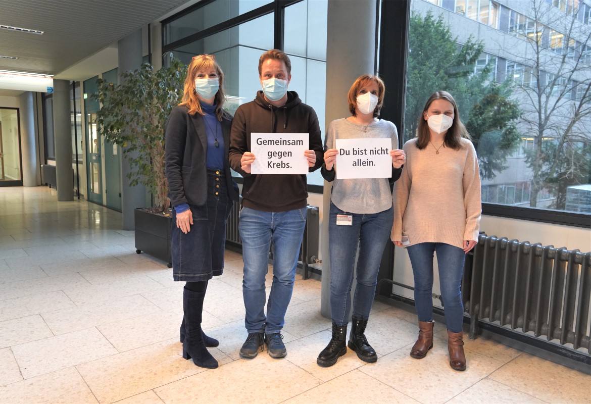 Mitarbeitende vom Team des Onkologischen Pflegerischen Konsiliardienst halten Schilder hoch, auf denen steht: "Gemeinsam gegen Krebs. Du bist nicht allein.". 