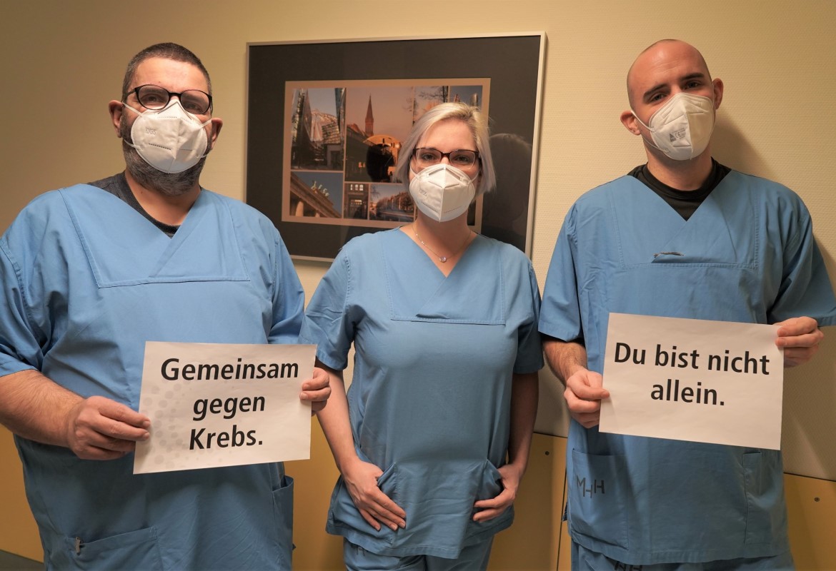 Das Wund- und Stomateam steht auf der Station und hält ein Schild hoch, auf dem steht: "Gemeinsam gegen Krebs. Du bist nicht allein."