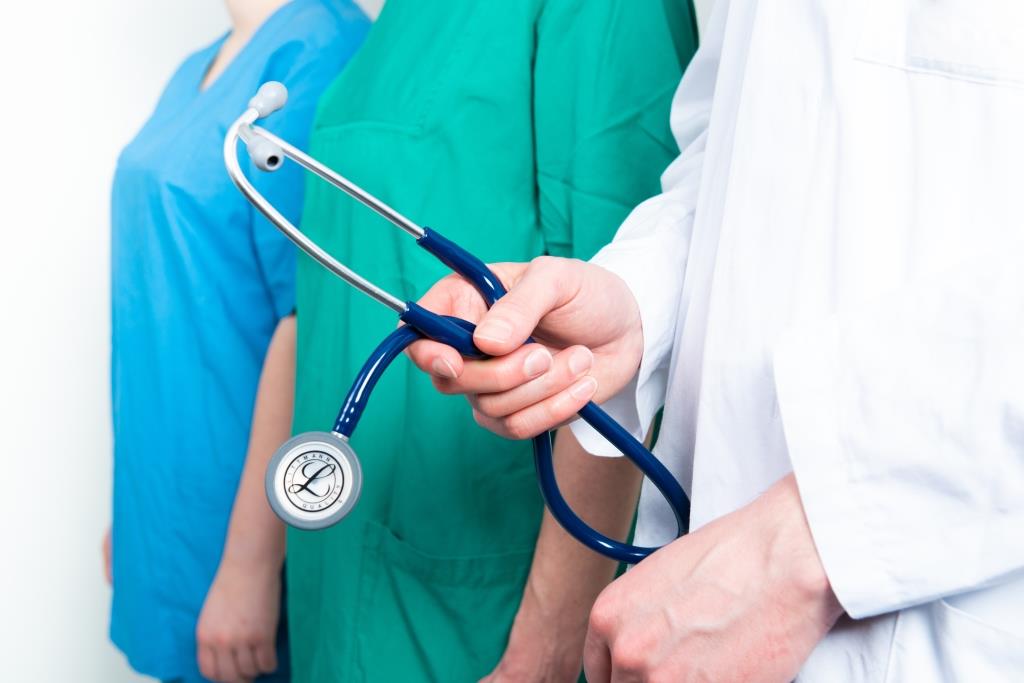 Drei medizinische Fachkräfte stehen nebeneinander. Eine Person im weißen Kittel hält ein Stethoskop.