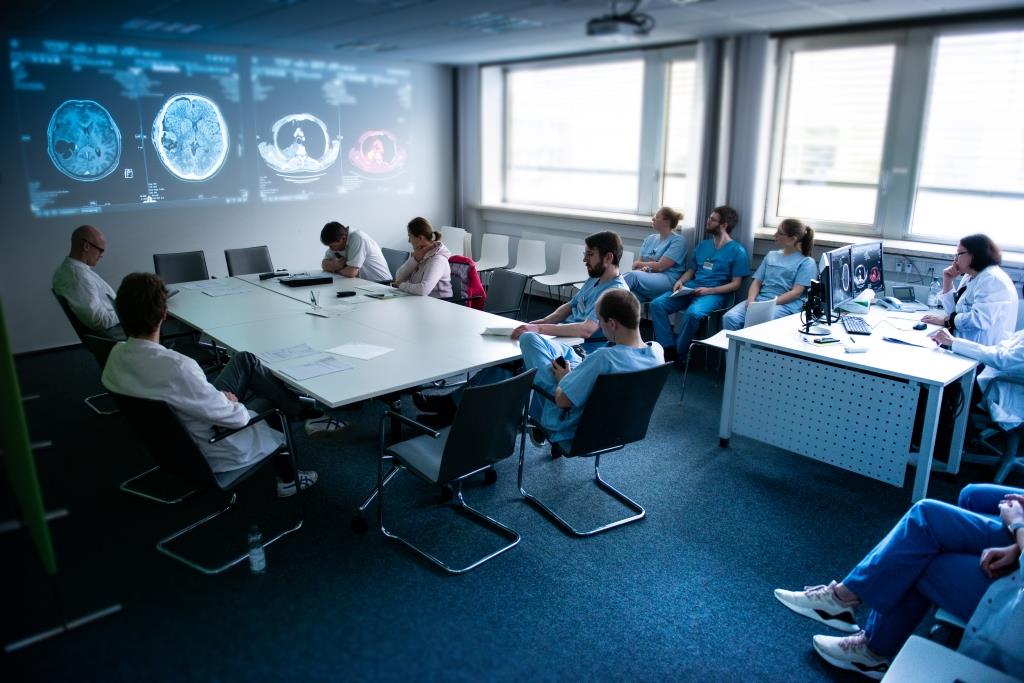 Ein Raumfoto in dem mehrere Ärztinnen und Ärzte sitzen und sich im Rahmen des Molekularen Tumorboards besprechen. An einer Wand sind CT Bilder projiziert.