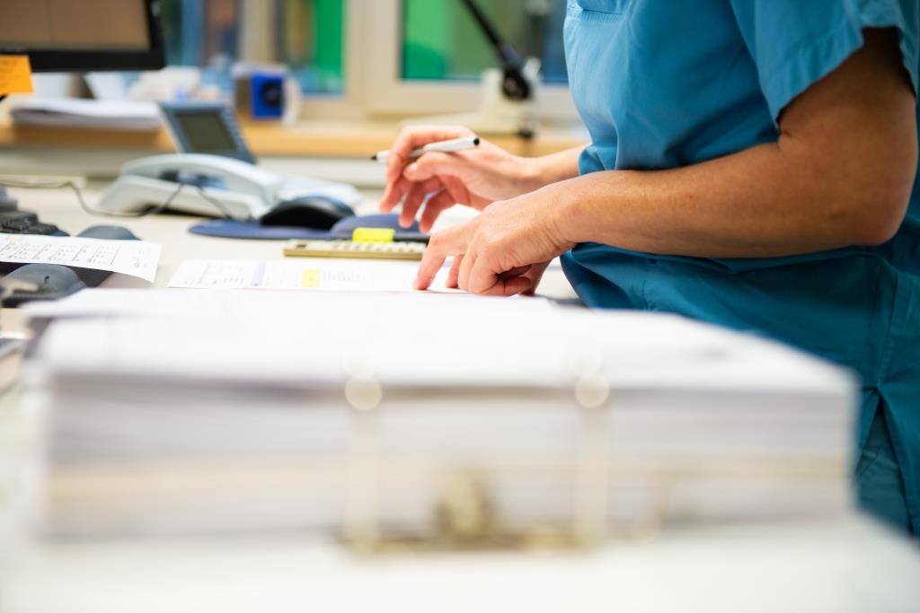 Eine Studynurse im Studienbüro macht sich Notizen. Neben ihr liegt ein Ordner mit Dokumenten.