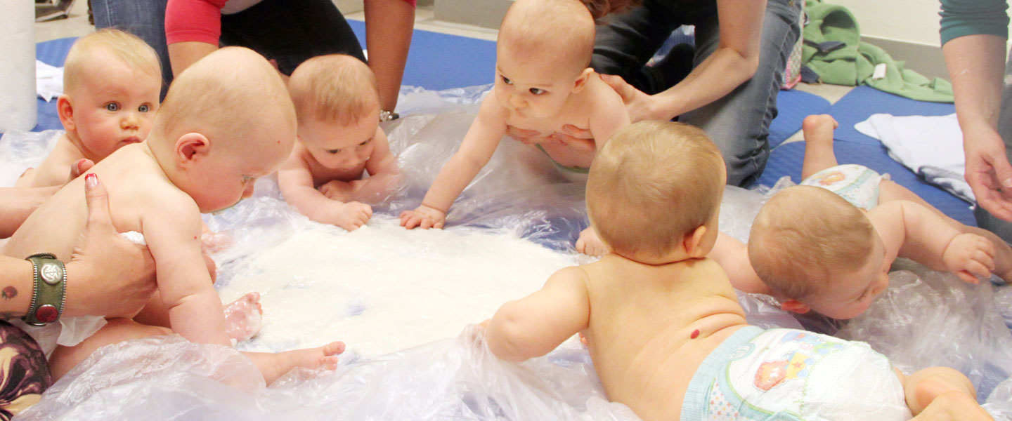 sechs Babys im Kreis, von ihren Müttern gehalten, beim Spielen