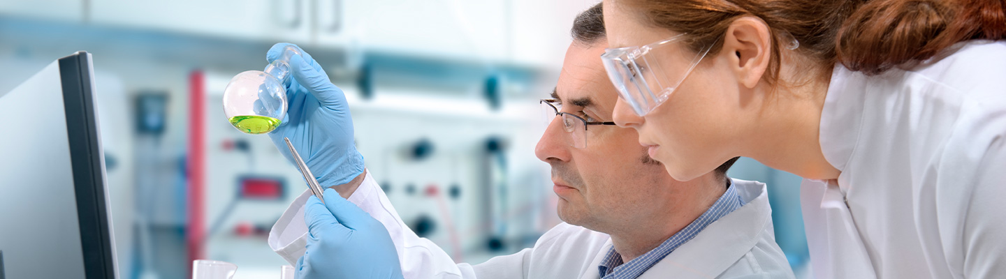 Ein Mann und eine Frau untersuchen eine farbige Flüssigkeit im Labor.