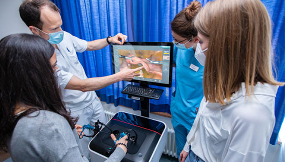 Arzt zeigt drei Studentinnen den Umgang mit OP-Simulator