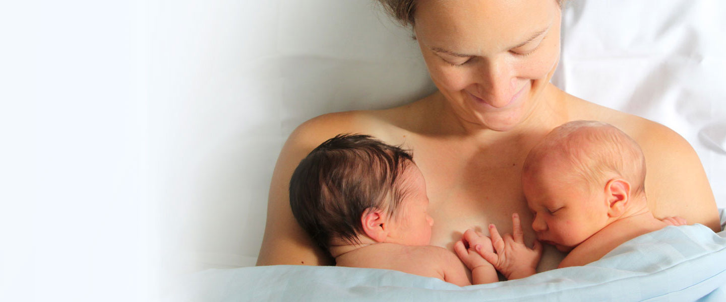 Bonding: Mutter mit ihren neugeborenen Zwillingen im Hautkontakt