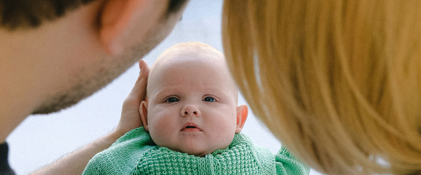 Baby sieht zwischen den Köpfen der Eltern hindurch den Betrachter an