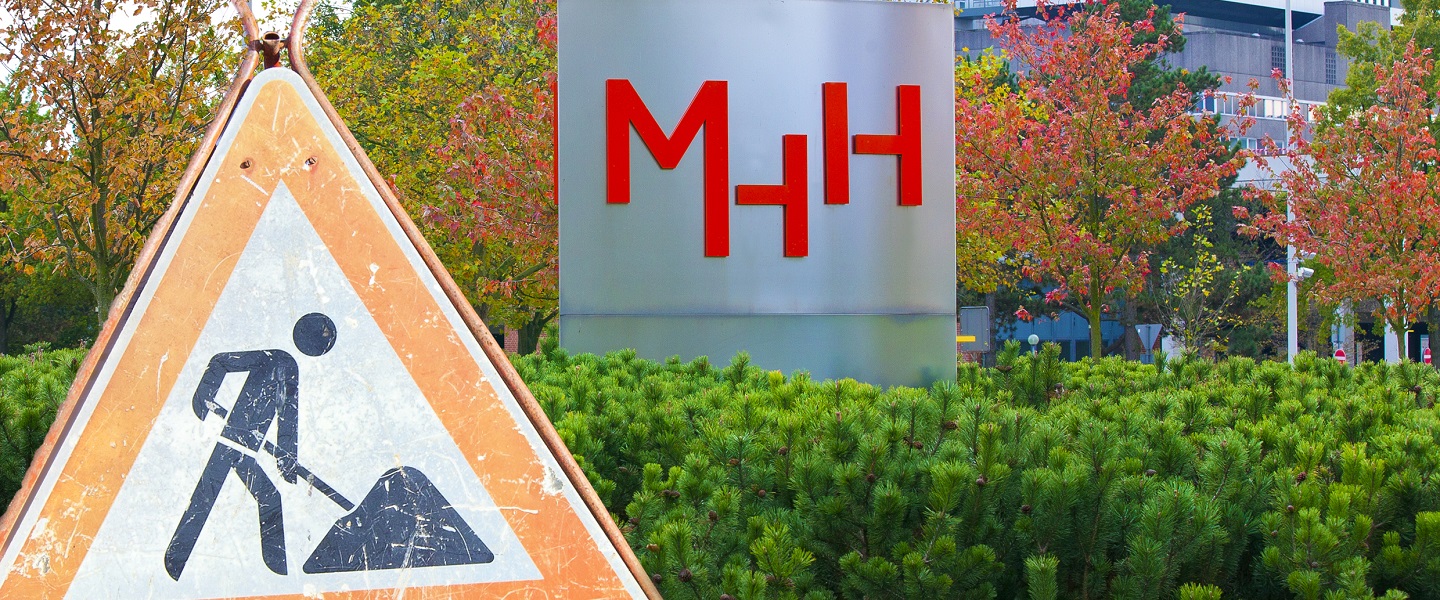 Das Bild zeigt die MHH-Stele (silberne Stele mit rotem MHH-Logo) und ein Baustellenschild. Copyright: Kaiser, Karin/Stabsstelle Kommunikation/MHH