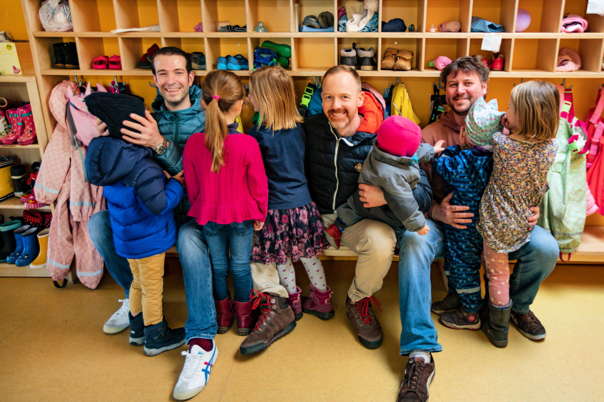 Drei Väter mit ihren Kinder im Garderobenbereich der Kita