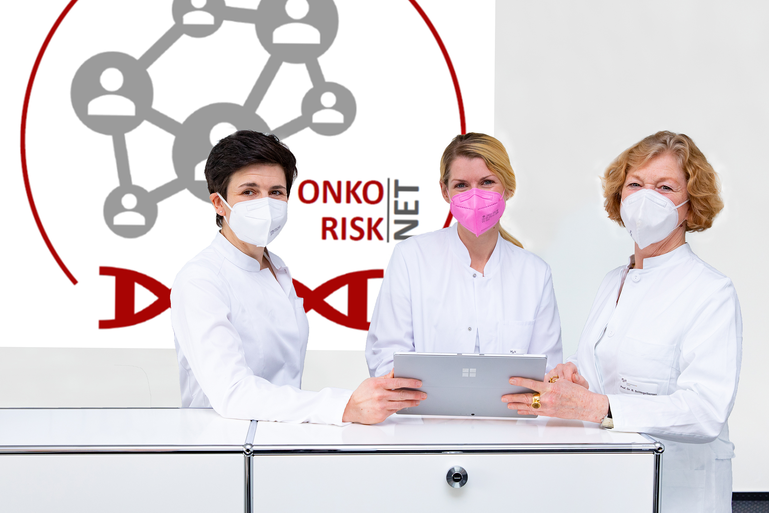 Three physicians holding a tablet in front of the logo of OnkoRisk NET.
