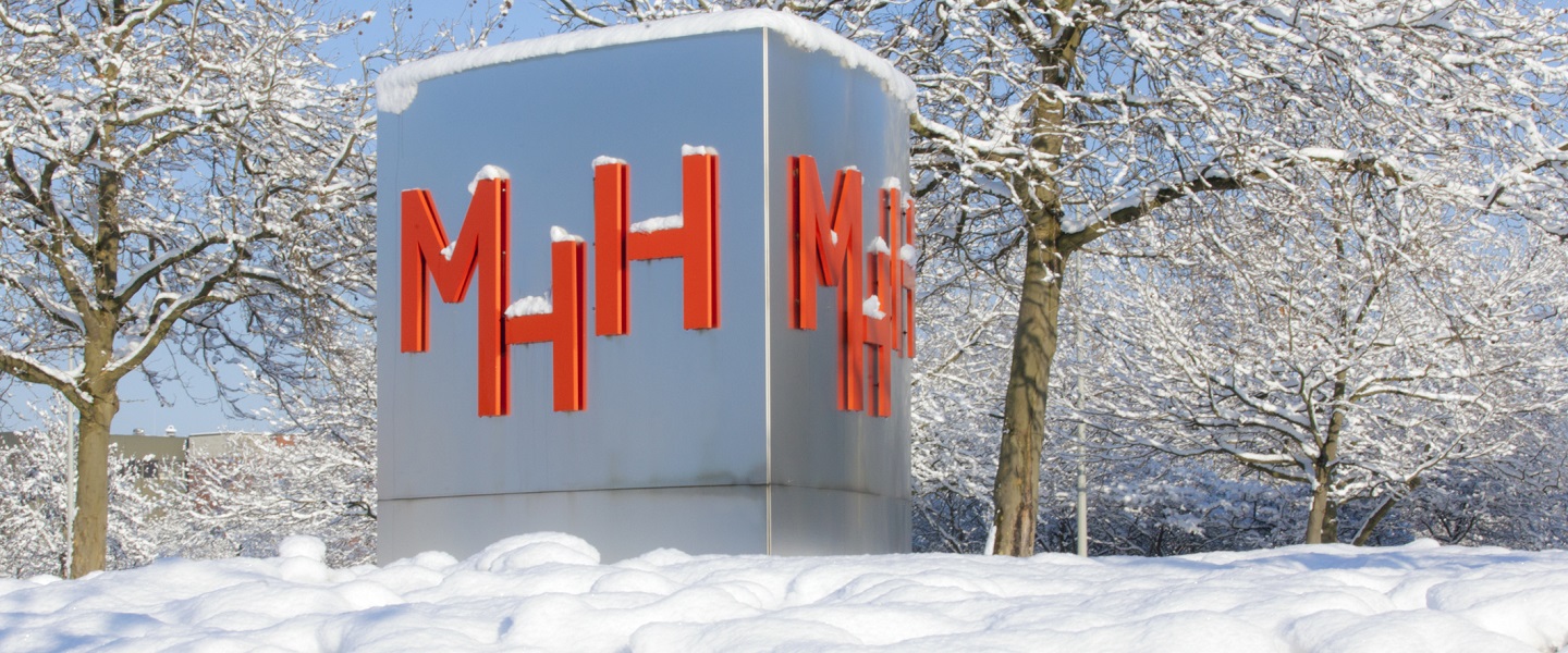 Das Bild zeigt die MHH Stele (silberne Stele mit rotem MHH-Logo) im Winter mit Schnee sowohl im Vordergrund als auch auf der Stele selbst. Copyright: Kaiser, Karin/Stabsstelle Kommunikation/MHH