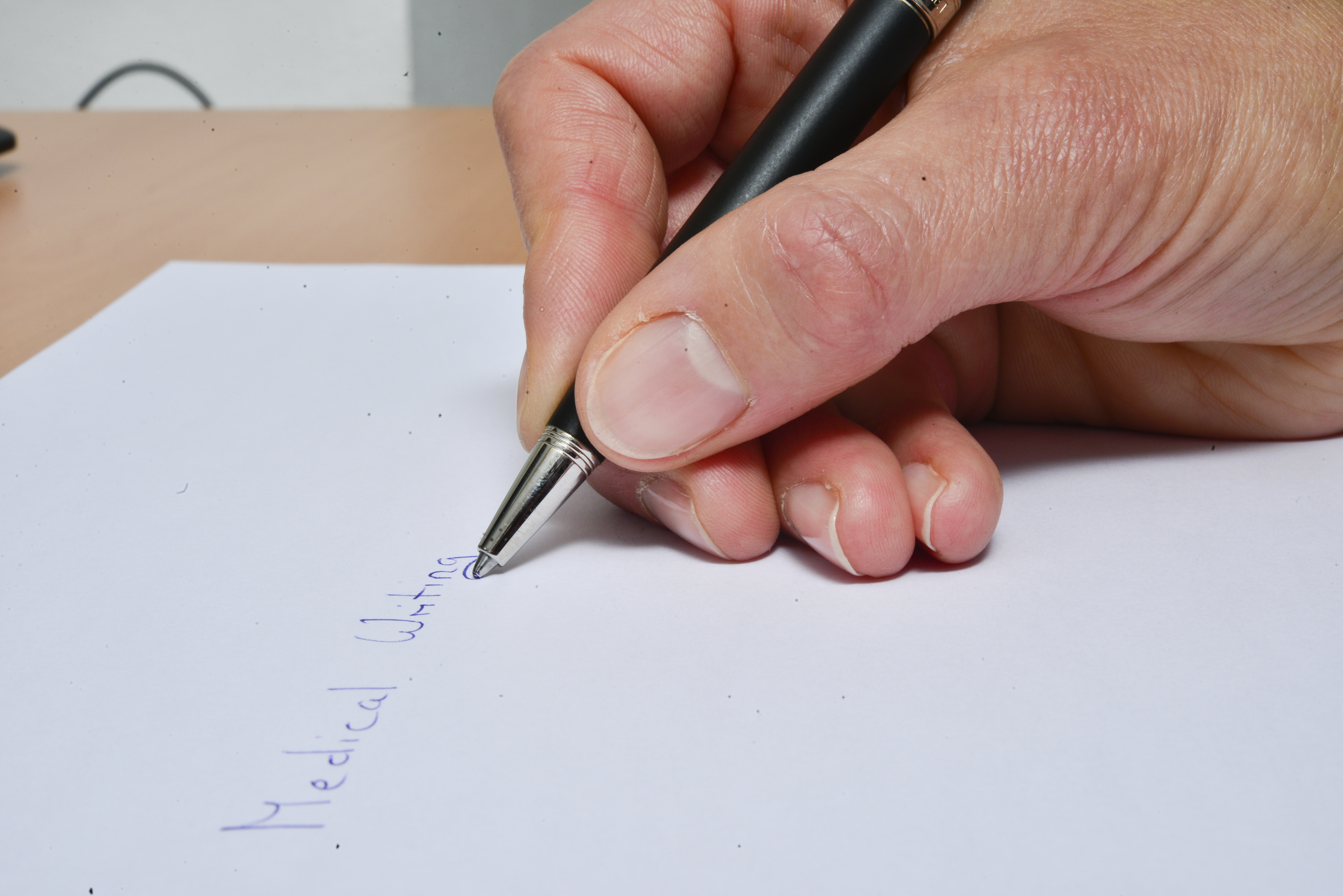 Hand die mit einem Kugelschreiber auf einem weissen Blatt Medical Writing schreibt