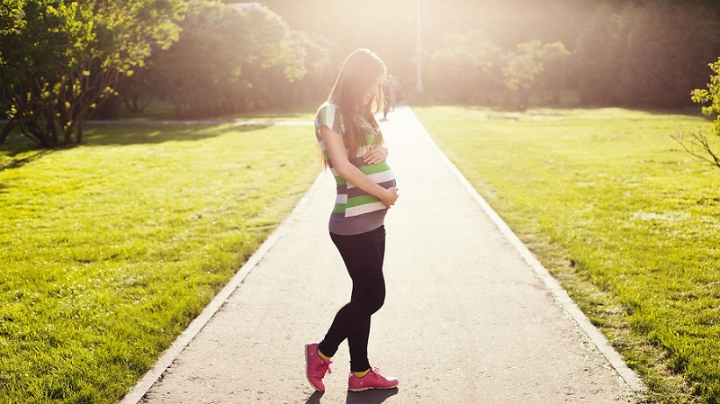 Das Bild zeigt eine schwangere junge Frau im Grünen.